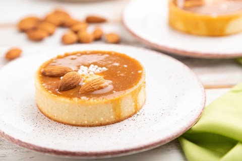 Sweet tartlets with almonds and caramel cream with cup of coffee on a white wooden background and