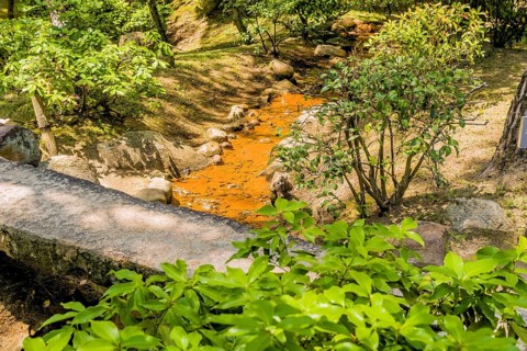 Small creek flowing under concrete footbridge in Japanese garden park in Hiroshima, Japan, Asia