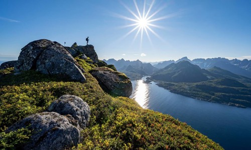 Mountaineer on the summit of Dronningsvarden or Stortinden, behind sea and fjord Umvagsundet,