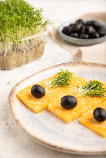 Marble cheese with olives and watercress microgreen on gray concrete background and linen textile.