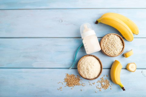 Powdered milk and oatmeal, banana baby food mix, infant formula, pacifier, bottle, spoon on blue