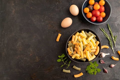Rigatoni colored raw pasta with tomato, eggs, spices, herbs on black concrete background. Top view,