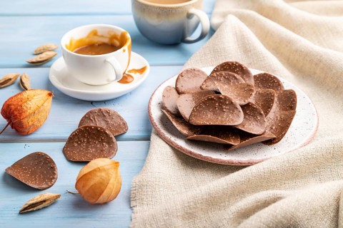 Chocolate chips with cup of coffee and caramel on a blue wooden background and linen textile. side