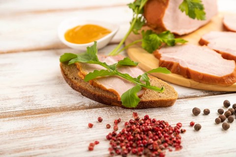 Smoked pork ham on cutting board with pepper and herbs on white wooden background. Side view, close