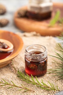 Pine cone jam with herbal tea on gray wooden background and linen textile. Side view, close up,