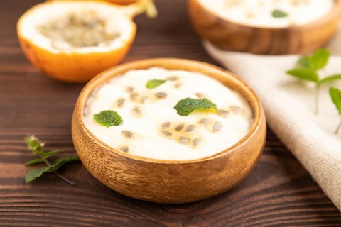 Yoghurt with granadilla and mint in wooden bowl on brown wooden background and linen textile. side