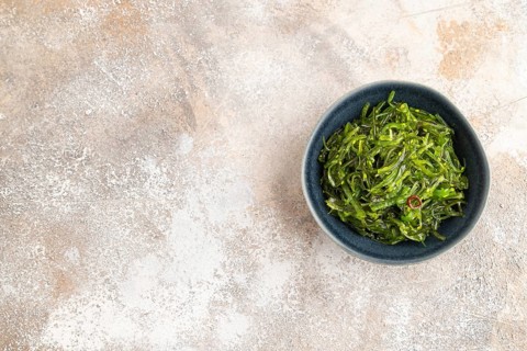 Chuka seaweed salad in blue ceramic bowl on brown concrete background. Top view, flat lay, copy