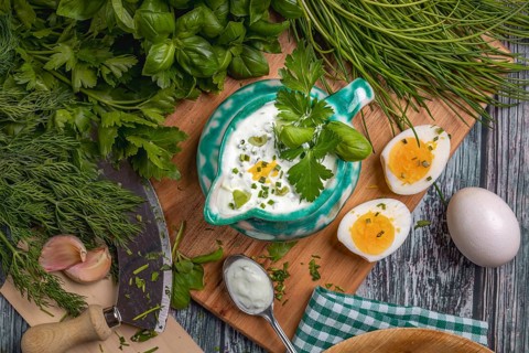 Herb dip in a turquoise ceramic jug, surrounded by fresh herbs and eggs