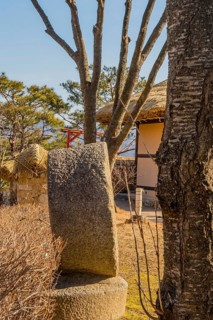 Side view of large millstone on display in public park with thatched roof building in background
