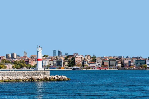 White lighthouse on pier in Bosphorus Strait with city skyline in background in Istanbul, Tuerkiye