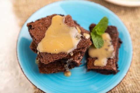 Chocolate brownie with caramel sauce with a cup of coffee on gray concrete background and linen