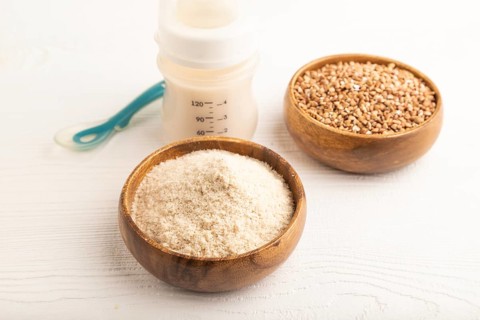 Powdered milk and buckwheat baby food mix, infant formula, pacifier, bottle, spoon on white wooden