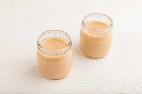 Baby puree with fruits mix, apple, banana infant formula in glass jar on white wooden background.