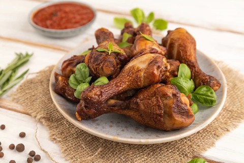Smoked chicken legs with herbs and spices on a ceramic plate with linen textile on a white wooden