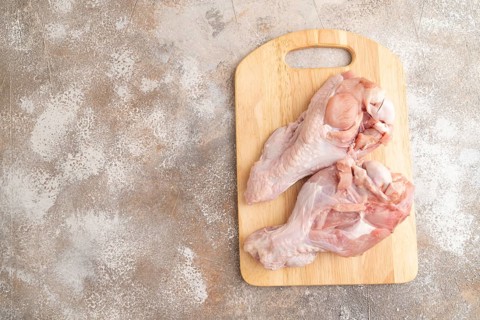 Raw turkey wing with herbs and spices on a wooden cutting board on a brown concrete background. Top