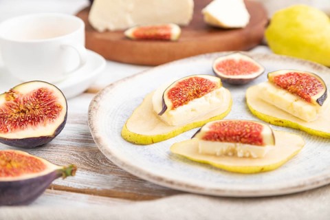 Summer appetizer with pear, cottage cheese, figs and honey on a white wooden background and linen