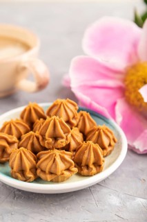 Homemade soft caramel fudge candies on blue plate and cup of coffee on gray concrete background,
