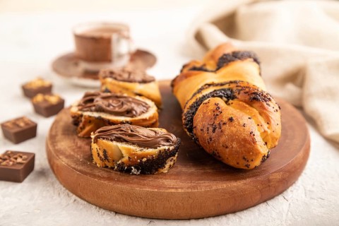 Homemade sweet bun with chocolate cream and cup of coffee on a gray concrete background and linen