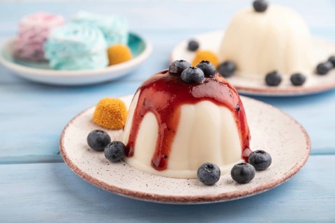 White milk jelly with blueberry jam on blue wooden background and blue linen textile. side view,