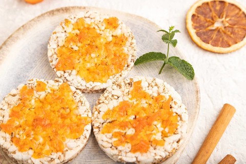 Carrot jam with puffed rice cakes on gray concrete background. Side view, close up, selective focus
