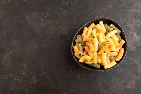 Rigatoni colored raw pasta with tomato, eggs, spices, herbs on black concrete background. Top view,