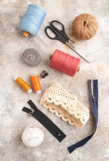 Sewing accessories: scissors, thread, thimbles, braid on brown concrete background. Top view, flat