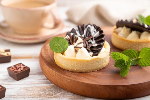 Sweet tartlets with chocolate and cheese cream with cup of coffee on a white wooden background and