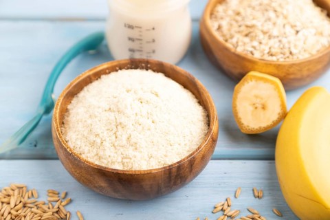 Powdered milk and oatmeal, banana baby food mix, infant formula, pacifier, bottle, spoon on blue