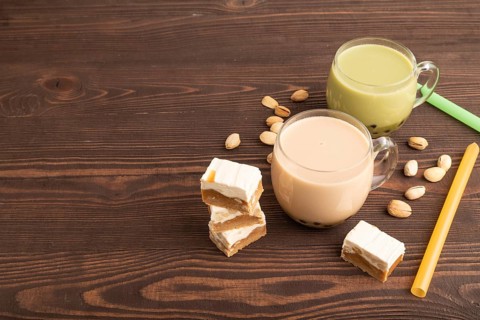 Bubble tea with pistachio and caramel in glass on brown wooden background. Healthy drink concept.