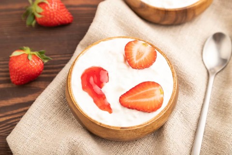 Grained cottage cheese with strawberry jam on brown wooden background and linen textile. side view,