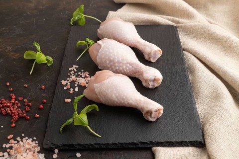 Raw chicken legs with herbs and spices on a black slate cutting board on a black concrete