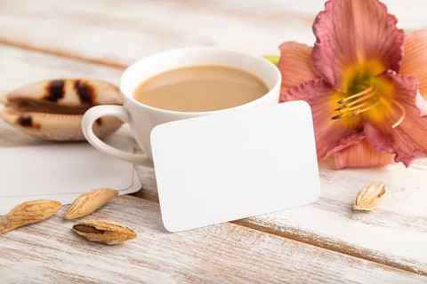 White paper business card mockup with purple day-lily flower and cup of coffee on white wooden