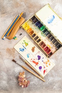 Drawing accessories set: brushes, pencils, watercolor on brown concrete background. Top view, flat