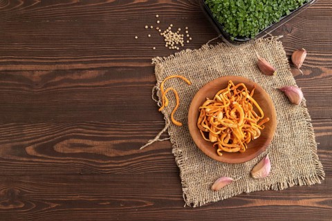 Fresh Cordyceps militaris mushrooms on brown wooden background with microgreen, herbs and spices.