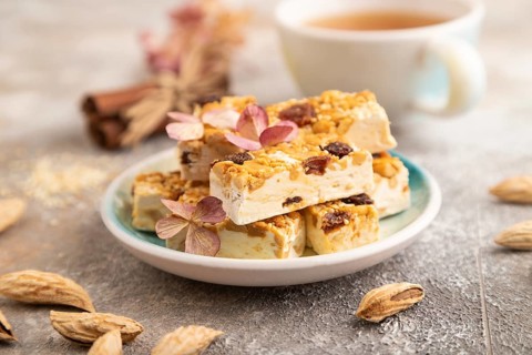Traditional candy nougat with nuts and sesame with cup of green tea on brown concrete background.
