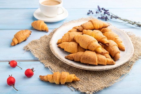 Homemade bagel roll with cup of coffee on a blue wooden background and linen textile. side view,