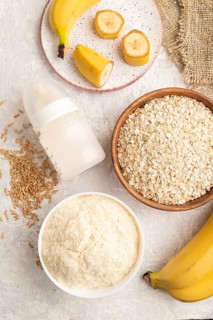 Powdered milk and oatmeal, banana baby food mix, infant formula, pacifier, bottle, spoon on gray