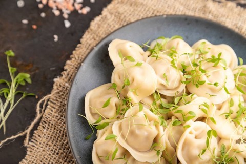Dumplings with pepper, salt, herbs, microgreen on black concrete background and linen textile. Top