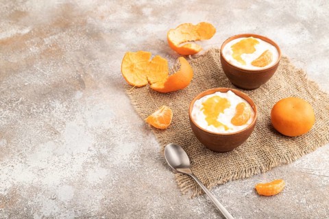 Grained cottage cheese with tangerine jam on brown concrete background and linen textile. side