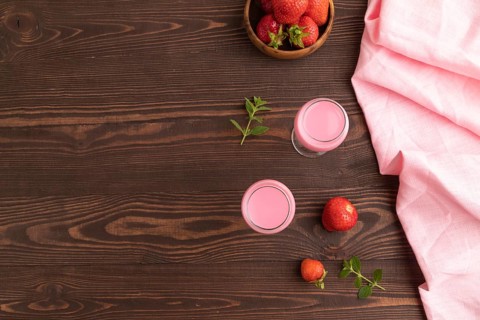 Sweet strawberry liqueur in glass on a brown wooden background and pink textile. top view, copy