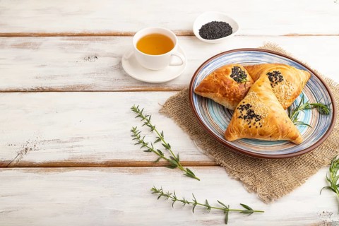 Homemade asian pastry samosa, cup of green tea on white wooden background and linen textile. side