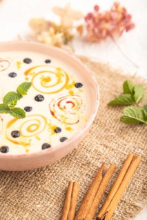 Yoghurt with bilberry and caramel in ceramic bowl on gray concrete background and linen textile.