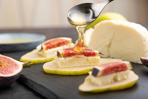 Summer appetizer with pear, cottage cheese, figs and honey on slate board on a black concrete