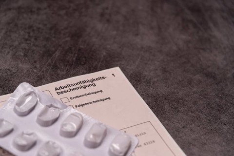 Blister pack with pills next to a certificate of incapacity for work on a grey stone slab, studio