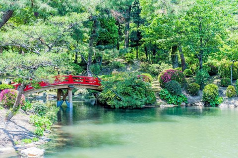 Red wooden footbridge over man made pond in Japanese garden in Hiroshima, Japan, Asia