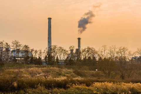 Large column of smoke rising from tall white smokestack in rural community in South Korea