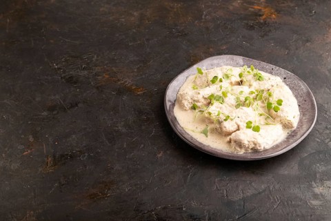 Stewed chicken fillets with coconut milk sauce and rucola microgreen on black concrete background.