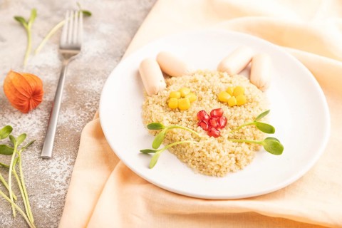 Funny mixed quinoa porridge, sweet corn, pomegranate seeds and small sausages in form of cat face