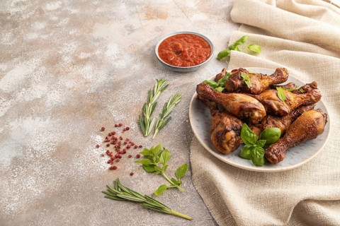 Smoked chicken legs with herbs and spices on a ceramic plate with linen textile on a brown concrete