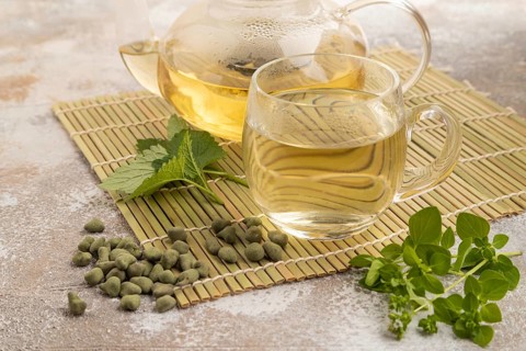 Green oolong tea with herbs in glass on brown concrete background. Healthy drink concept. Side
